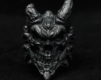 May include: A black, detailed, demonic skull ring with horns and sharp teeth.