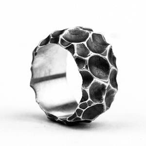 Puede incluir: Un anillo de plata con un diseño texturizado y orgánico. El anillo está hecho de metal y tiene una superficie rugosa y desigual.