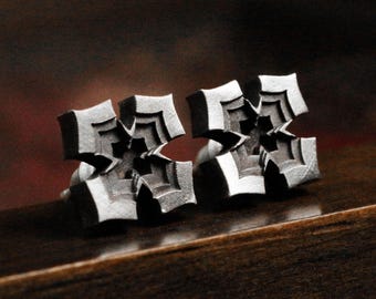 May include: A pair of silver cufflinks with a geometric, starburst design. The cufflinks are made of metal and have a polished finish.
