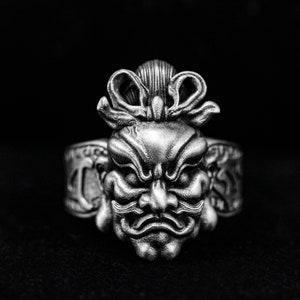 Op de afbeelding: Een zilveren ring met een gedetailleerd ontwerp van een Japans demonenmasker met een strik erboven.