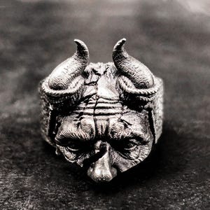 Puede incluir: Un anillo de plata con un diseño detallado de la cara de un demonio con cuernos.