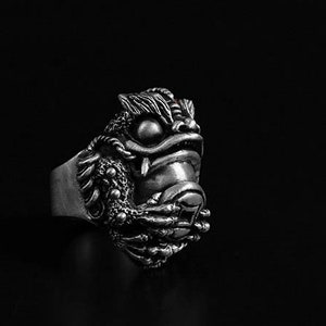 Puede incluir: Un anillo de plata con un diseño detallado de cabeza de león. La boca del león está abierta, revelando dientes afilados. El anillo es una pieza llamativa con detalles intrincados.