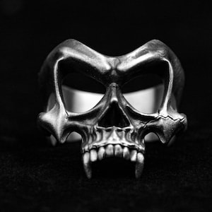 Op de afbeelding: Een zilveren schedelring met scherpe tanden en gedetailleerde kenmerken. De ring is ontworpen in gotische stijl en heeft een donkere en edgy esthetiek.