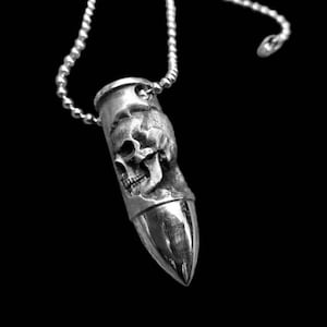 Könnte beinhalten: Eine silberne Kugel-Anhänger-Kette mit einem detaillierten Totenkopf-Design. Der Anhänger ist an einer silbernen Kette befestigt.