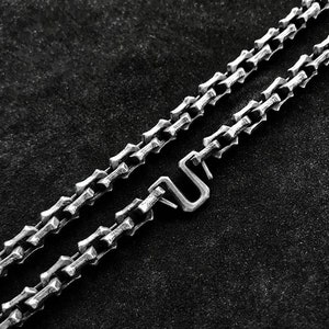 May include: A silver chain necklace with a unique, chunky link design. The chain has a simple, sturdy clasp.