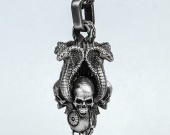 May include: A silver pendant necklace featuring a skull surrounded by three cobras with their heads raised. The pendant has a detailed design and a dark finish.