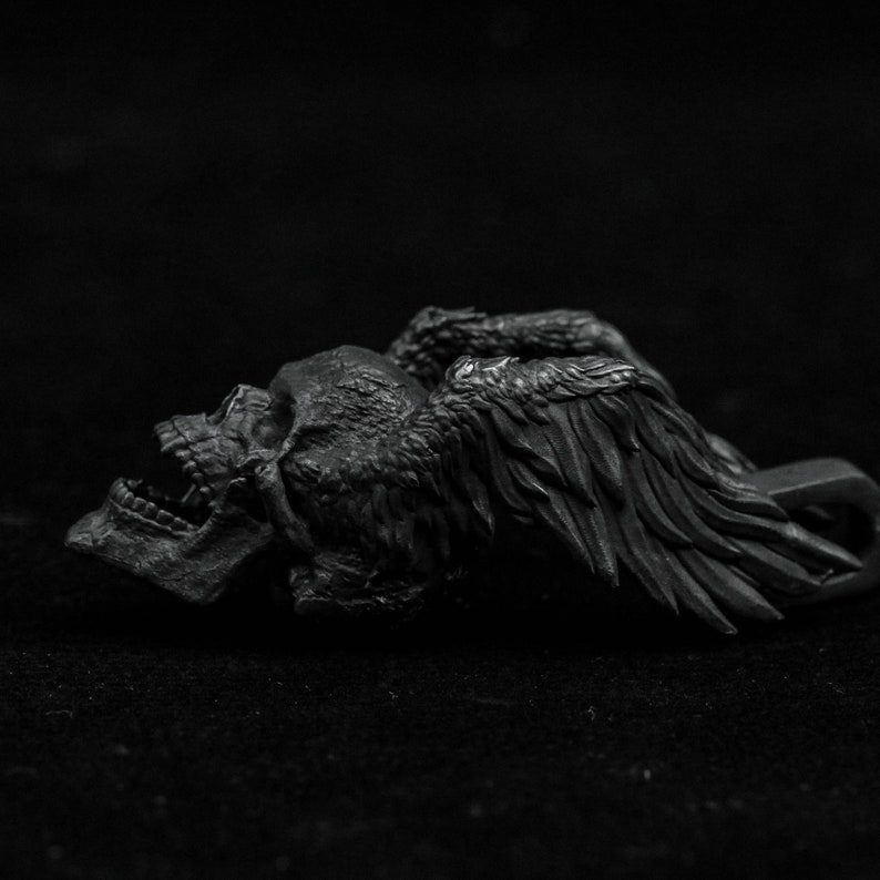 May include: A black skull with wings, the skull is open mouthed and the wings are spread out. The skull and wings are made of a smooth, dark material.