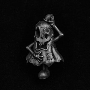 May include: A black and white ghost figurine with a stitched face and a hat. The ghost is standing on a black surface.