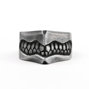 May include: A silver ring with a detailed design of a mouth with sharp teeth.