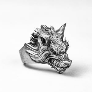 Könnte beinhalten: Ein silberner Ring mit einem detaillierten Wolfskopf-Design. Der Wolf hat den Mund offen und zeigt scharfe Zähne. Der Ring ist aus Metall gefertigt und hat eine strukturierte Oberfläche.