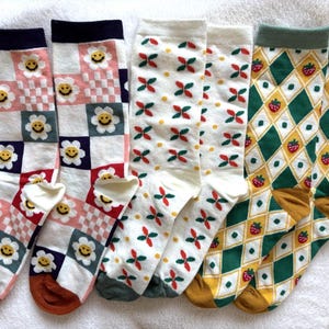 May include: A set of six colourful socks with different patterns. The socks feature a white background with various designs, including flowers, strawberries, and geometric shapes. The socks are made of a soft, comfortable material and are perfect for everyday wear.