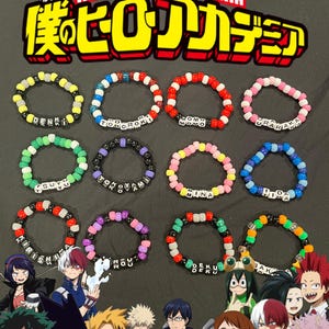 Puede incluir: Pulseras de cuentas coloridas con nombres de personajes de My Hero Academia. Cada pulsera presenta un esquema de color y un nombre diferente, como "Denki" y "Todoroki". El logotipo de My Hero Academia está en la parte superior.