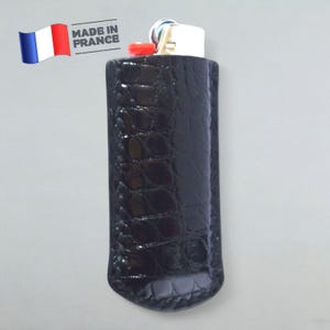 Puede incluir: Estuche para encendedor de cuero negro con un patrón de cocodrilo. El estuche está hecho en Francia.