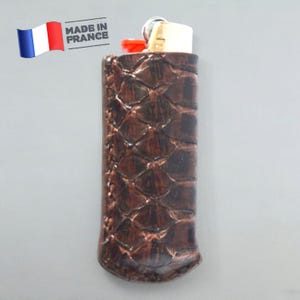 Peut inclure: Un étui à briquet en cuir marron avec un motif texturé. L'étui est fabriqué en France.