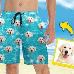 May include: Turquoise swim trunks with a repeating pattern of a golden retriever's face. The trunks have a drawstring closure and pockets. The background shows a beach scene with a yellow arrow pointing to a photo of the dog.