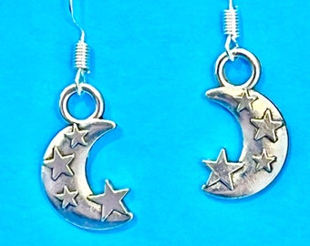 May include: A pair of silver crescent moon earrings with small stars on each moon. The earrings are on a blue background.