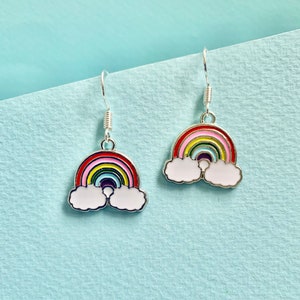 May include: A pair of silver dangle earrings featuring a rainbow and cloud design. The rainbow is multi-coloured with red, orange, yellow, green, blue, indigo, and violet. The clouds are white.