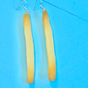 Könnte beinhalten: Ein Paar Hängeohrringe in Form von Pommes Frites. Die Ohrringe sind aus hellgelbem Material und haben silberne Haken.