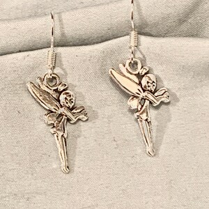 Puede incluir: Un par de pendientes de plata con un dise&ntilde;o de hada. Las hadas est&aacute;n representadas con alas, un vestido y una cara delicada.