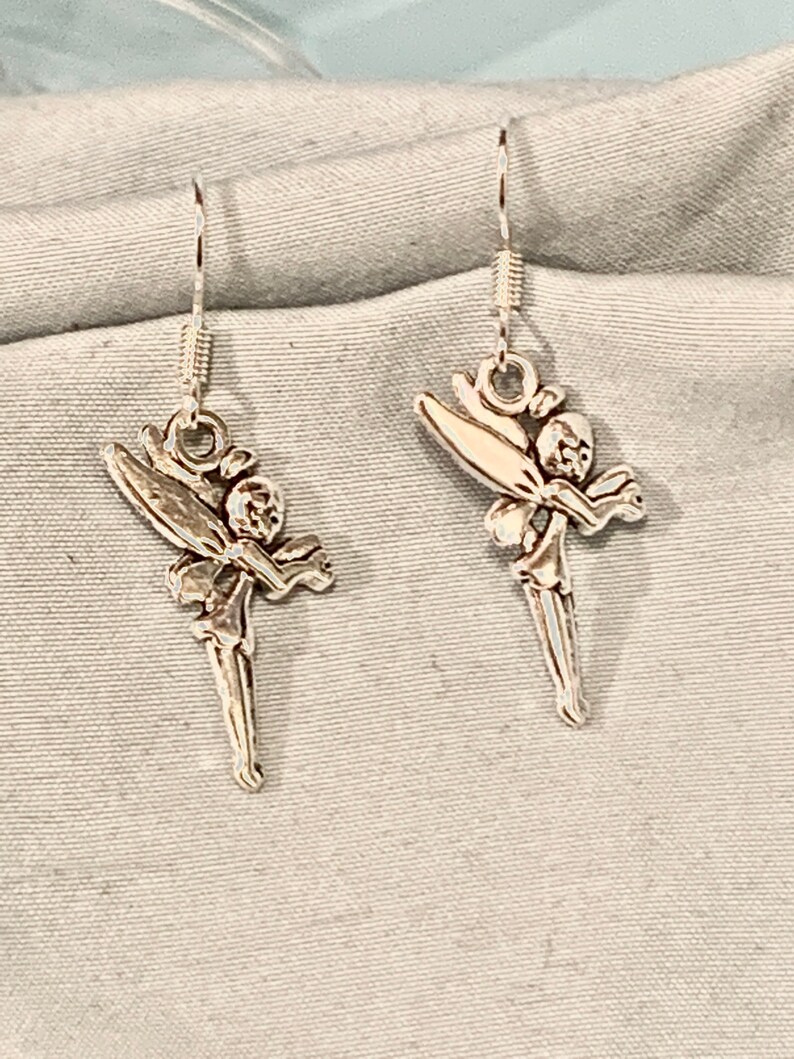 Puede incluir: Un par de pendientes de plata con un dise&ntilde;o de hada. Las hadas est&aacute;n representadas con alas, un vestido y una cara delicada.