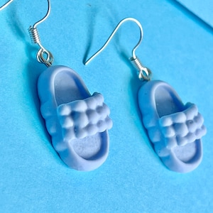 May include: A pair of light blue dangle earrings shaped like puffy slippers with silver hooks.