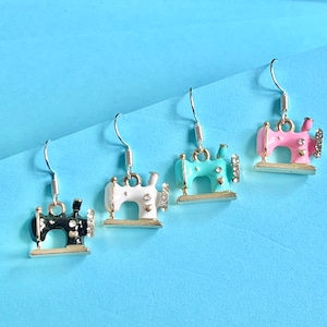 May include: Four pairs of earrings featuring a sewing machine design. The earrings are silver with gold accents and come in black, white, light blue, and pink.