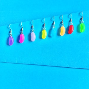 May include: Eight pairs of dangle earrings with jelly bean shaped charms in various colours, including purple, pink, light blue, yellow, green, and red.