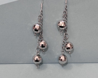 May include: Silver dangle earrings with three round, faceted, silver beads on each earring.