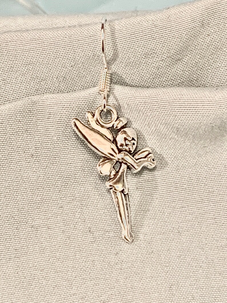 Puede incluir: Pendientes de aro de plata con un dise&ntilde;o de hada. El hada est&aacute; representada con alas, un vestido fluido y una cara delicada.