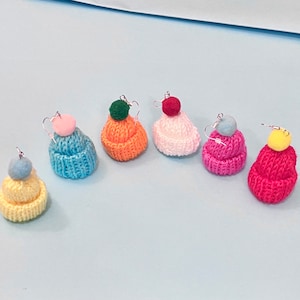 May include: Seven pairs of knitted beanie hat earrings with pom poms in various colors, including pink, blue, yellow, red, orange, and white.