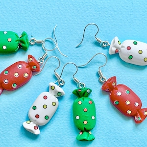 May include: Candy-shaped earrings in green, red, and white with colorful polka dots. The earrings have silver-colored fish hook ear wires. The candy earrings are a fun and playful accessory.