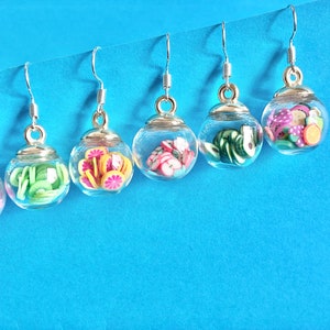 May include: Five pairs of silver dangle earrings with clear glass jars filled with colorful miniature fruit slices. The fruit slices include kiwi, lime, orange, apple, and watermelon.