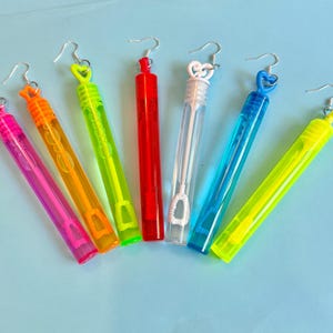 May include: An assortment of colorful bubble wands. The wands are in various colors, including pink, orange, green, red, white, blue, and yellow. Each wand has a clear plastic tube and a heart-shaped or swirl-shaped top.