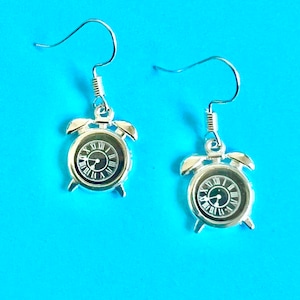 May include: A pair of silver alarm clock earrings with black clock faces. The earrings have a hook fastening.
