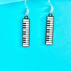 May include: A pair of silver earrings with black and white piano key charms. The earrings are hanging against a bright blue background.