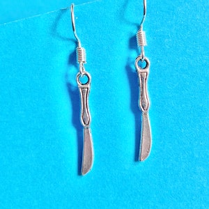 May include: A pair of silver earrings shaped like a butter knife. The earrings have a simple design and are a fun and unique accessory.