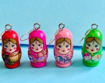 May include: Four pairs of wooden nesting doll earrings. The dolls are painted in red, pink, pink and green. Each doll has a different design. The earrings are made with silver hooks.