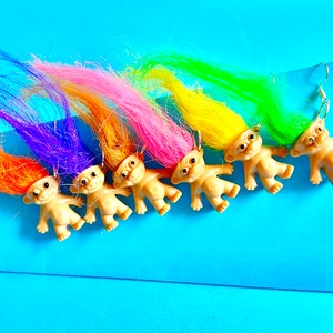 May include: Five troll doll earrings with rainbow colored hair. The trolls are all wearing the same expression and have the same body shape. The earrings are made of plastic and are about 2 inches tall.