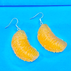 Puede incluir: Un par de pendientes de plata con abalorios de fruta cítrica naranja. Los abalorios tienen forma de segmento de naranja con una superficie texturizada.
