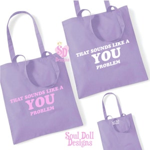 Könnte beinhalten: Zwei lilafarbene Tragetaschen mit dem Text "That sounds like a you problem" in weißer und rosa Schrift. Die kleinere Tasche hat den Text in weiß und die größere Tasche hat den Text in rosa. Beide Taschen haben den Text "Soul Doll Designs" unten.