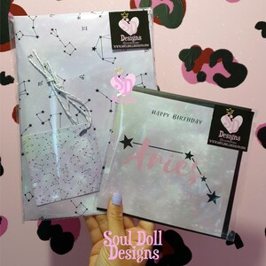 Puede incluir: Una tarjeta de cumplea&ntilde;os rosa y blanca con un borde negro y las palabras "Feliz cumplea&ntilde;os" y "Aries" en rosa. La tarjeta est&aacute; decorada con una constelaci&oacute;n de estrellas y un coraz&oacute;n rosa con las palabras "Soul Doll Designs" en blanco.