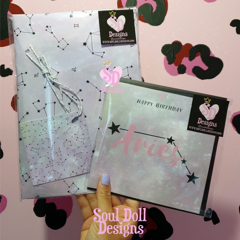 Puede incluir: Una tarjeta de cumplea&ntilde;os rosa y blanca con un borde negro y las palabras "Feliz cumplea&ntilde;os" y "Aries" en rosa. La tarjeta est&aacute; decorada con una constelaci&oacute;n de estrellas y un coraz&oacute;n rosa con las palabras "Soul Doll Designs" en blanco.