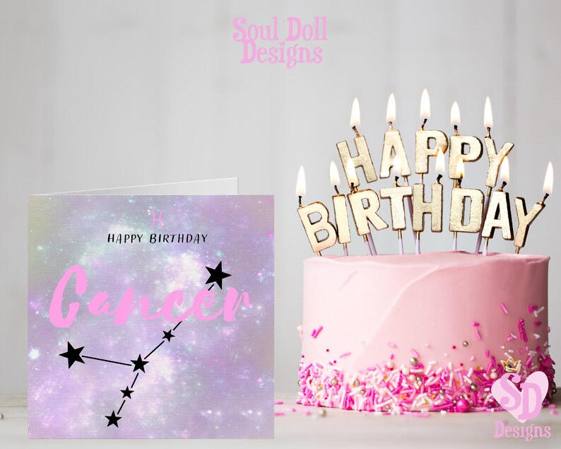 Puede incluir: Una tarjeta de cumplea&ntilde;os rosa con un fondo de galaxia p&uacute;rpura y blanco que presenta el signo del zod&iacute;aco C&aacute;ncer y el texto "Feliz cumplea&ntilde;os C&aacute;ncer". La tarjeta est&aacute; junto a un pastel rosa con velas doradas que deletrean "Feliz cumplea&ntilde;os".