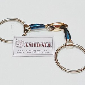 May include: A metal horse bit featuring two large circular rings connected by a jointed mouthpiece with blue and gold-toned metallic segments. A white rectangular tag is attached, displaying the text AMIDALE INDUSTRIES and website URLs.