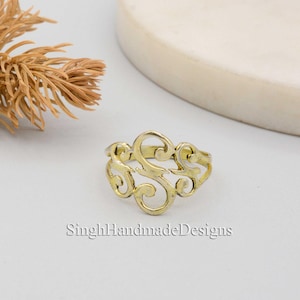 May include: A gold-toned ring featuring a decorative, openwork design in the shape of the letter "S".