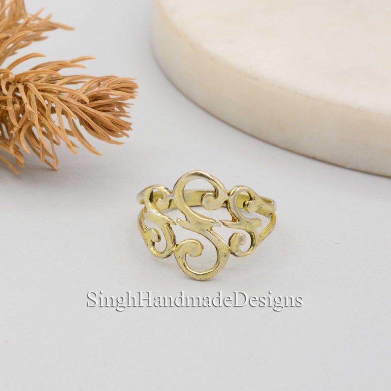 May include: A gold-toned ring with a decorative, openwork design in the shape of the letter "S".