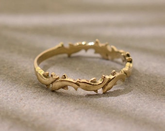 May include: A gold ring with a delicate, intricate design of swirling, leaf-like shapes. The ring is simple and elegant.