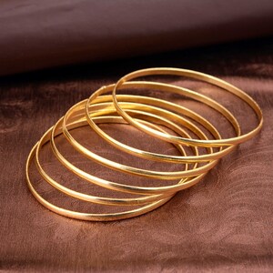 May include: A set of six gold-toned bangle bracelets. The bracelets are stacked on top of each other, creating a layered look.