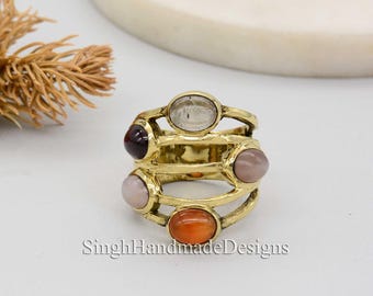 May include: Gold ring with five oval-shaped gemstones in shades of pink, orange, gray, and purple. The ring has a multi-layered design with three bands.