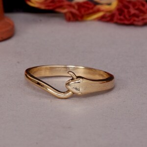 Puede incluir: Un anillo de color dorado con un diseño de serpiente. La cabeza de la serpiente está mirando al usuario y la cola se envuelve alrededor de la banda.